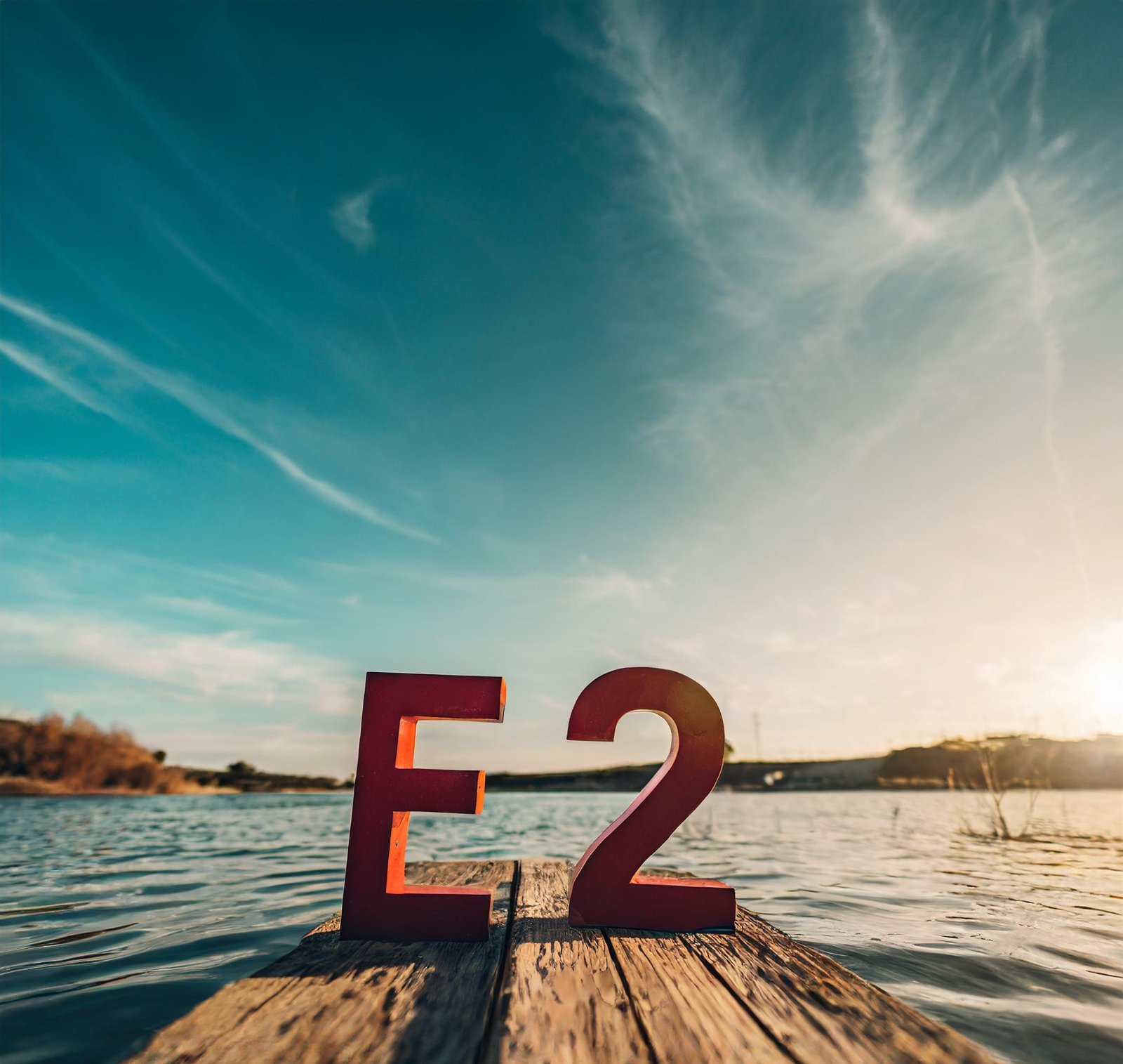 red wooden letters "E2" on a wood surface with a body of water in the background