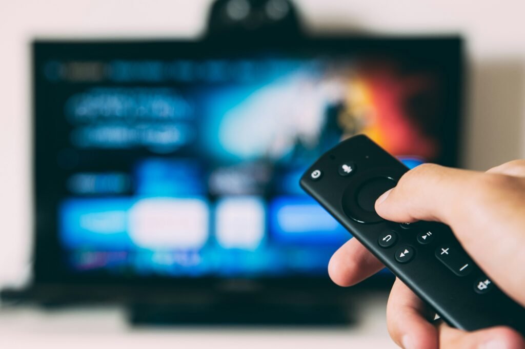 a hand holding a remote control in front of a television